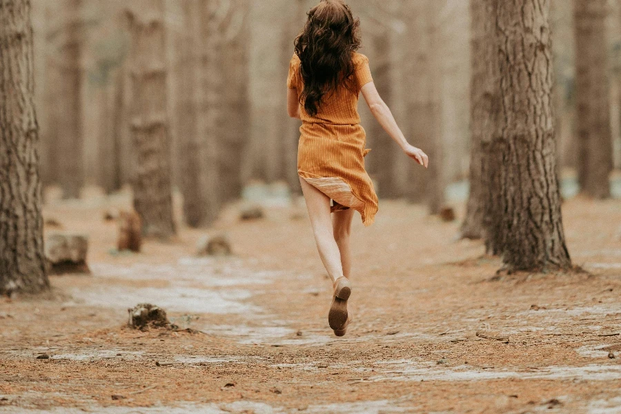 Adult woman running in dress among trees