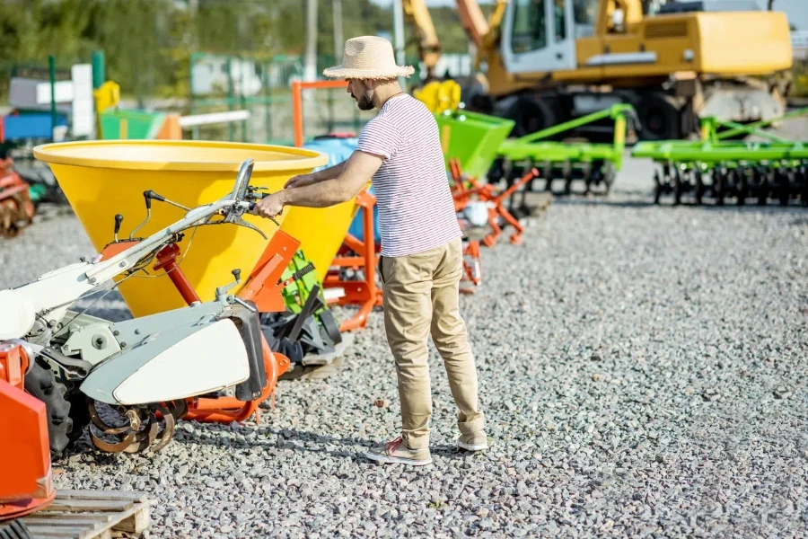 Agronomist choosing farm cultivator machine at the outdoor ground of the shop with agricultural machinery