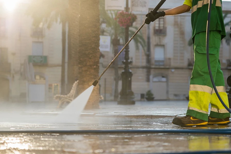 An unrecognizable worker uses a high-pressure water cleaner to remove dirt in the street