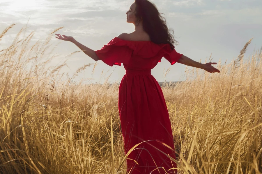 Attractive Woman in Long Red Dress Standing in Tall Grass and Greeting Sunlight