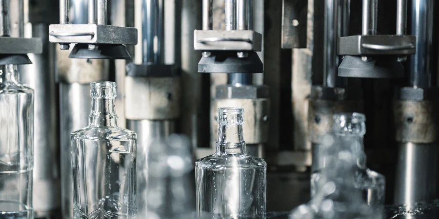 Automatic production line fills glass bottles with vodka drink in light workshop at manufacturing plant close view