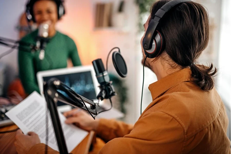 Back view of young man recording podcast on interview with beautiful and successful women in studio holding paper