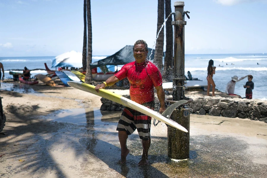 Black male carrying surfboard on beach