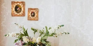 Ramo de flores florecientes con pétalos suaves cerca de una pared ornamental con pinturas en la casa