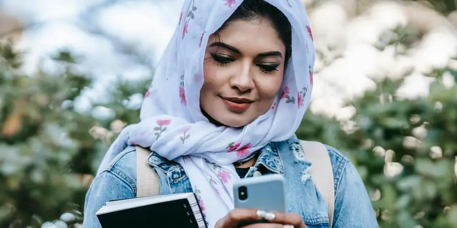 Mulher muçulmana alegre com smartphone por Keira Burton