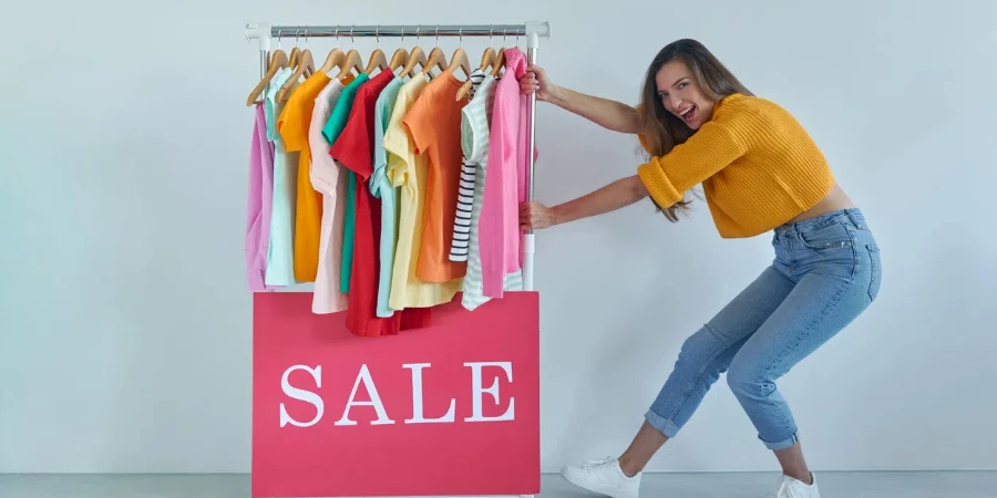 Cheerful young woman pulling a rack with colorful clothes