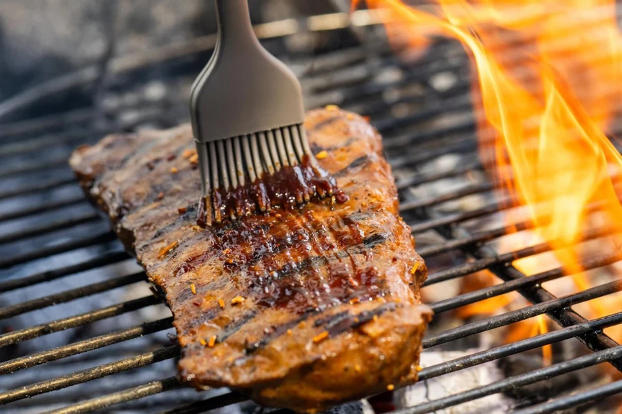 Close-up of brush applying barbeque sauce on roasted meat kept on barbecue grill.