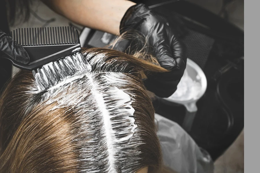 Close up of colorist dyes hair of woman with brush and foil in beauty salon