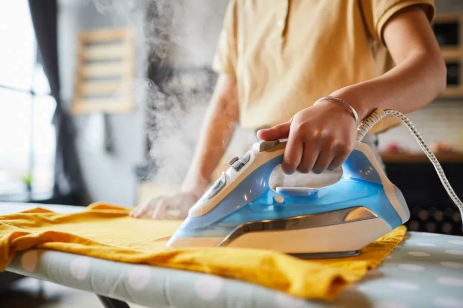 Close up of unrecognizable young woman ironing clothes at home, simple lifestyle and household chores concept, copy space