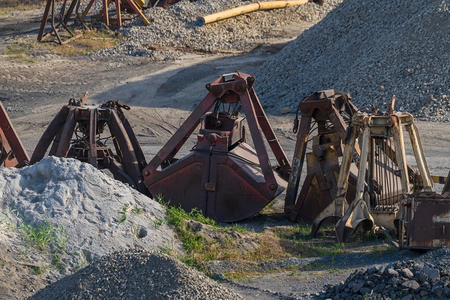 Close-up view of group of large shell buckets of bulk-handling crane lying on ground next to heaps of gravel in city port