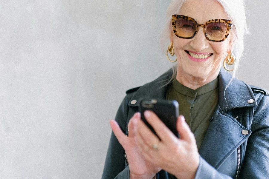 Crop happy senior female in stylish jacket touching screen