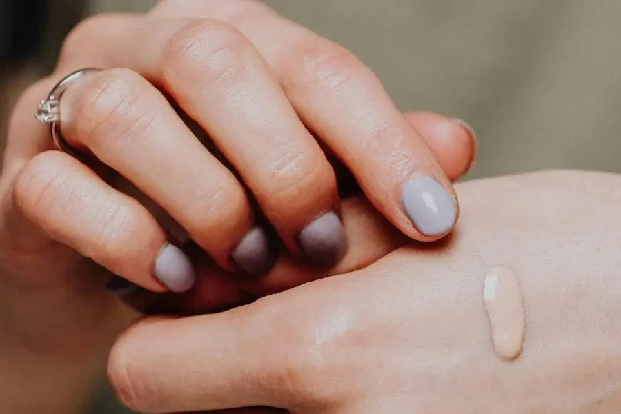 Crop unrecognizable female in casual clothes with manicured hands demonstrating drop of makeup foundartion on back of hand by Karolina Kaboompics