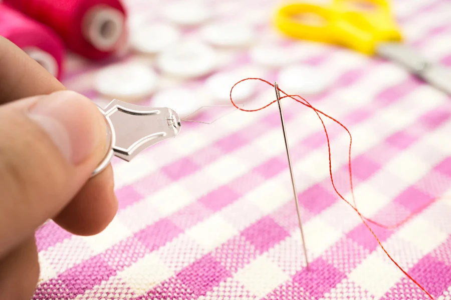 Easy push red thread pass the hole of sewing needle with threader, close up photo
