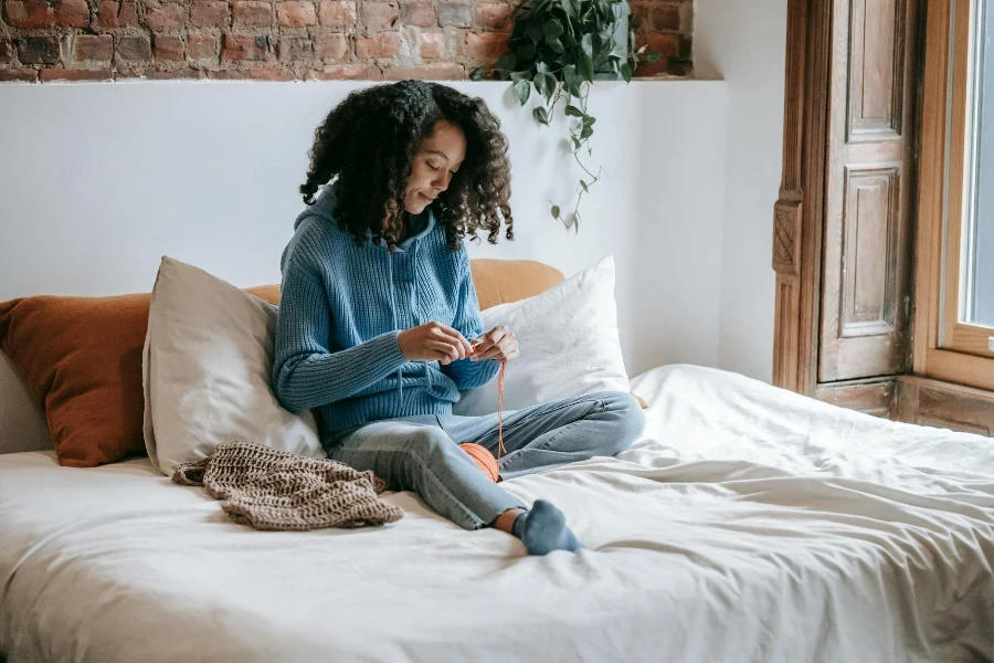 Ethnic artisan crocheting on bed in light house