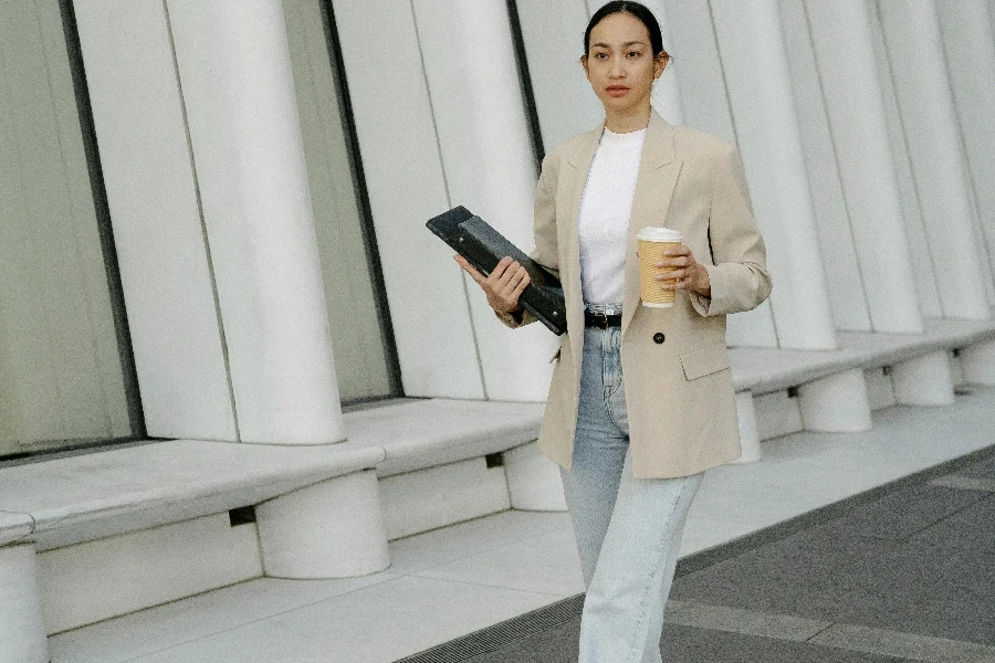 Ethnic woman carrying laptop with folder and cup of coffee