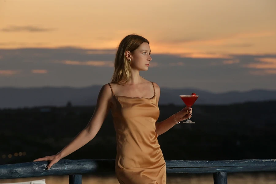 Fashionable young woman holding cocktail with beautiful sunset behind