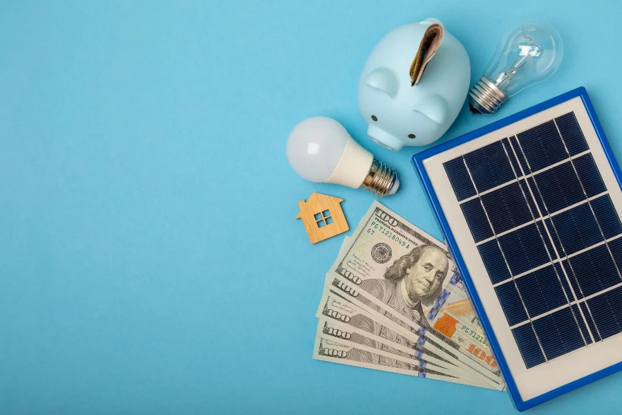 Flat lay composition with solar panel, led lamp, house model, money and piggy bank on blue background