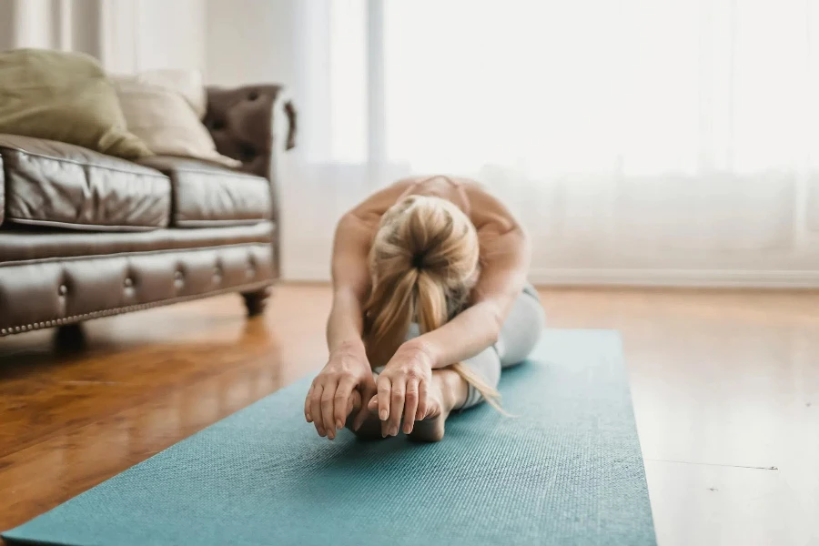 Flexible lady practicing Pascimottanasana yoga pose at home