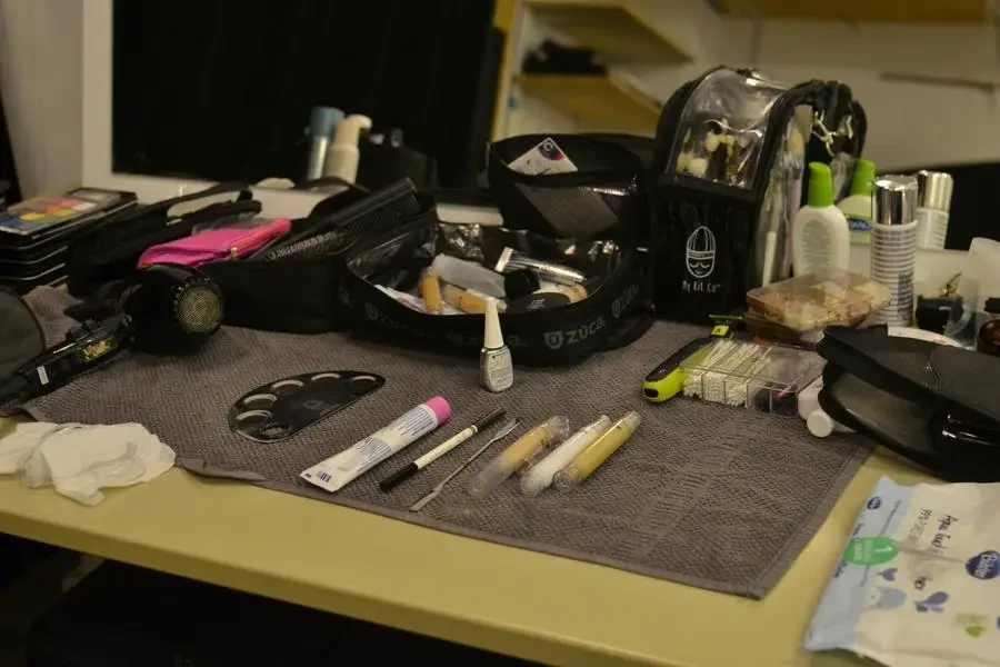 From above of hair dryer and cosmetic bags with various makeup supplies and products placed on table in dressing room by Skylar Kang