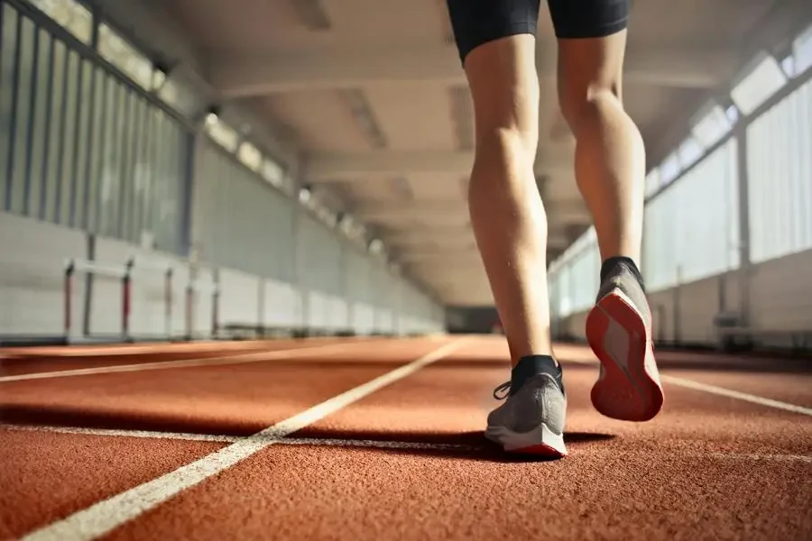 Van onder af agteraansig van gewas sterk hardloper wat langs die hardloopbaan in atletiekarena loop terwyl hy opwarmingsoefeninge doen tydens oefensessie deur Andrea Piacquadio