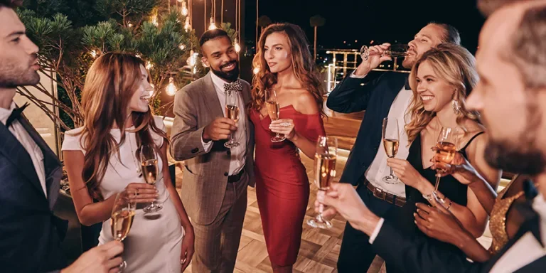 Grupo de hermosos jóvenes vestidos de forma formal comunicándose y sonriendo mientras pasan el tiempo en una fiesta de lujo.