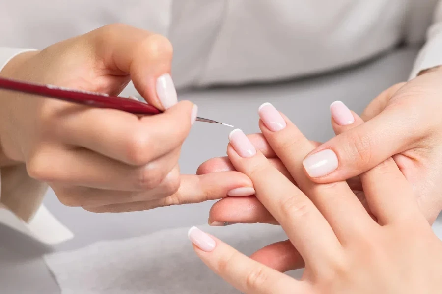 Hand of young woman receiving french manicure by beautician at nail salon