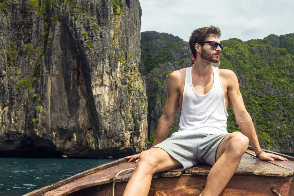 Handsome male cruising on retro wood boat by Andaman sea and behind him you can see Ko Phi Phi Lee Island in full glory