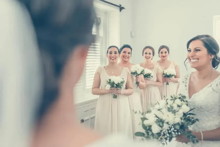 Happy women wearing elegant dresses standing with bouquets of flowers while congratulating unrecognizable blurred bride in veil during wedding ceremony by X L