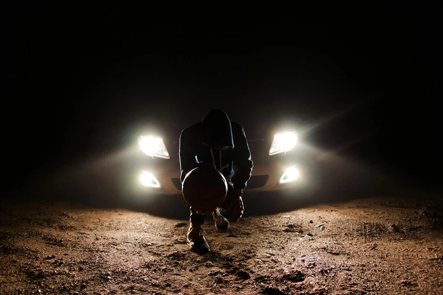 Man Against the Vehicle Headlight Squatting Holding Ball