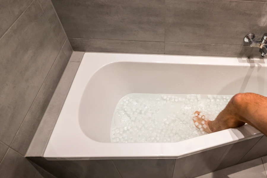 Man going into a bathtub filled with cold water and ice cubes for recovery