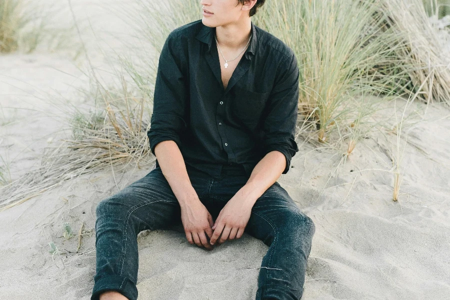 Man in Black Dress Shirt and Black Denim Jeans Sitting on Gray Sand