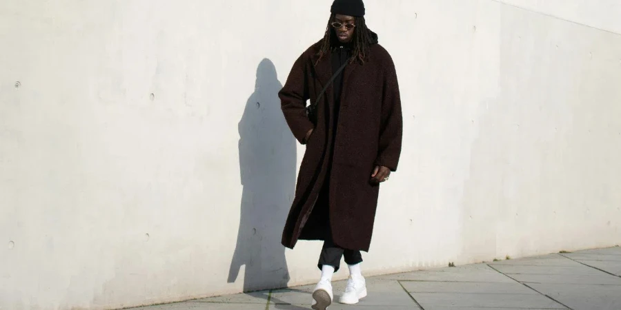 Man in a Brown Coat and a Beanie Standing against the Wall