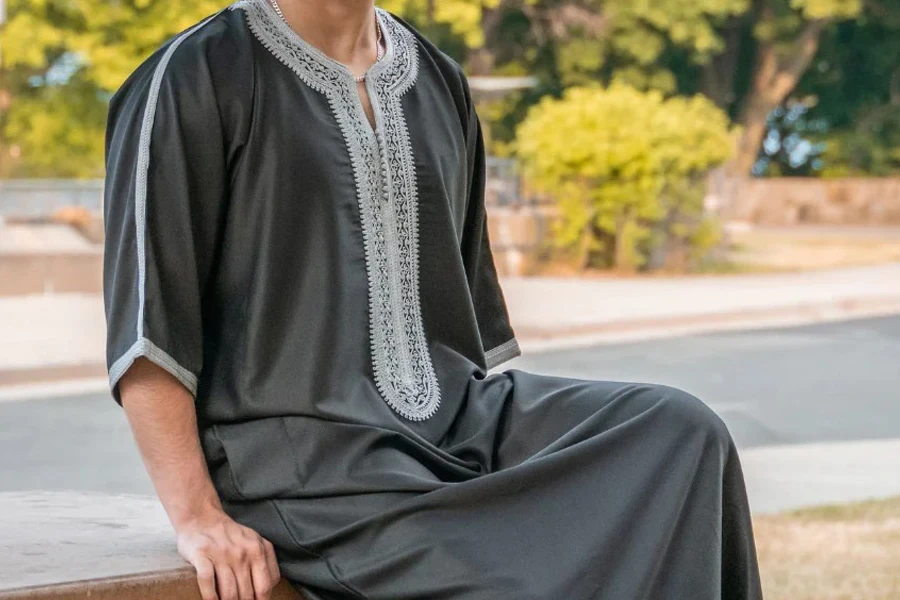 Man sitting on a fence in black Moroccan thobe