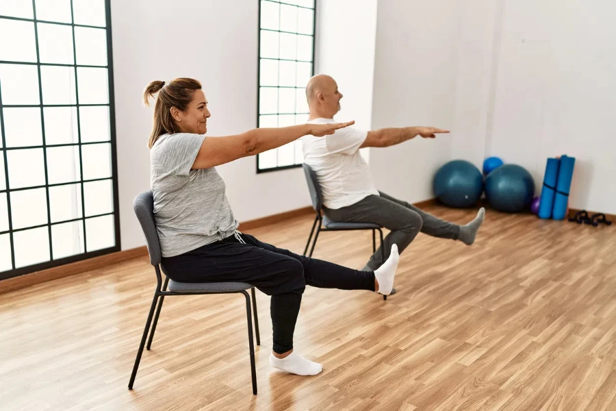Middle age hispanic couple stretching using chair at sport center