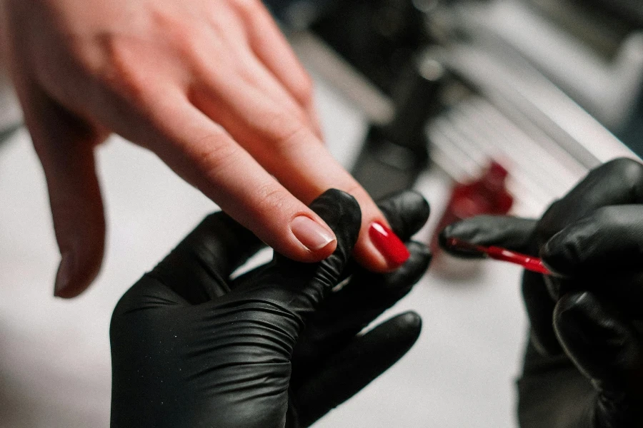 Person in Black Leather Gloves Holding Red Nail Polish