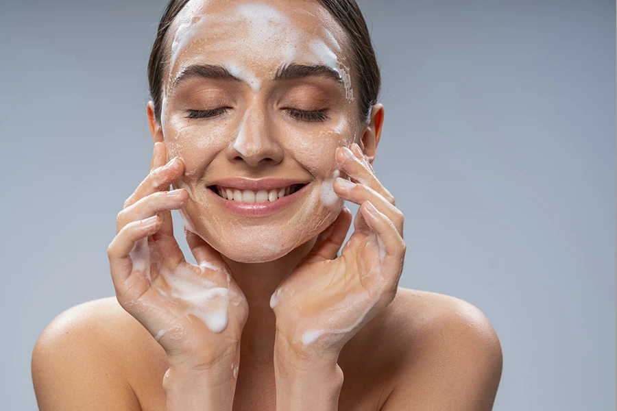 Portrait of smiling attractive woman touching face by hands while cleansing the skin from makeup