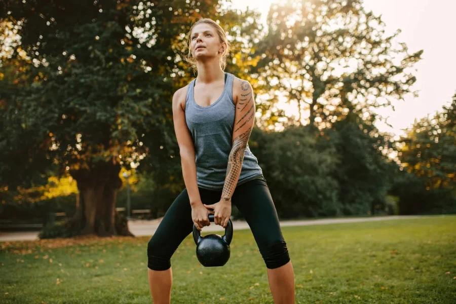 Portrait of strong young woman exercising with kettlebell weights in the park. Fit and muscular woman training at city park in morning