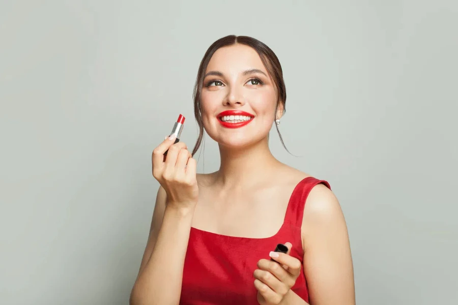 Pretty young woman holding red lipstick near lips