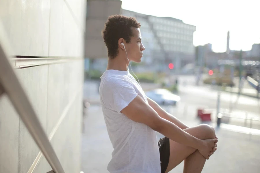 Side view of calm thoughtful African American male athlete in earphones and sportswear looking away and stretching leg