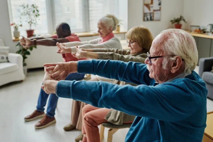 Side view of senior people doing exercises sitting on chairs in the morning in the room