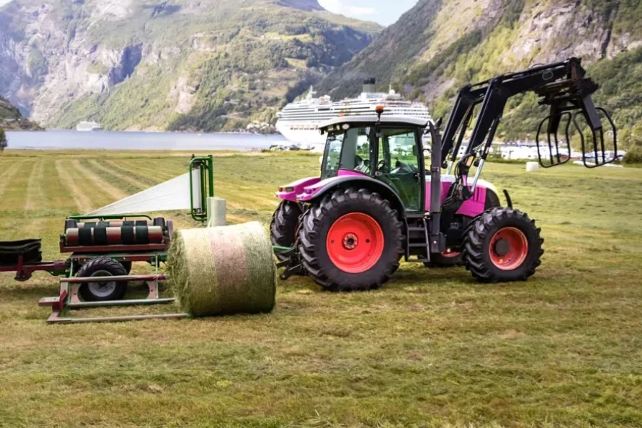 Small tractor with a round bale wrapper on a field in Geiranger