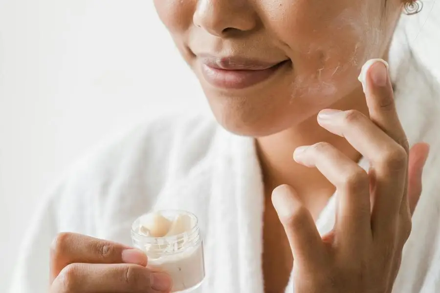 Smiling Woman Applying Facial Cream on Her Face by Greta Hoffman