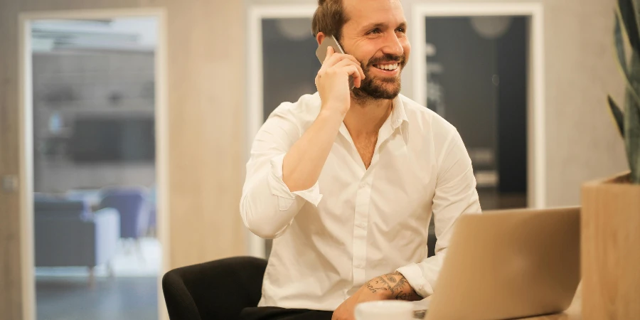 Smiling formal male with laptop chatting via phone