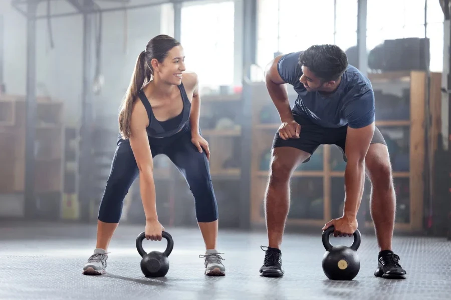 Strong, wellness couple doing kettlebell weight exercise, workout or training inside a gym 