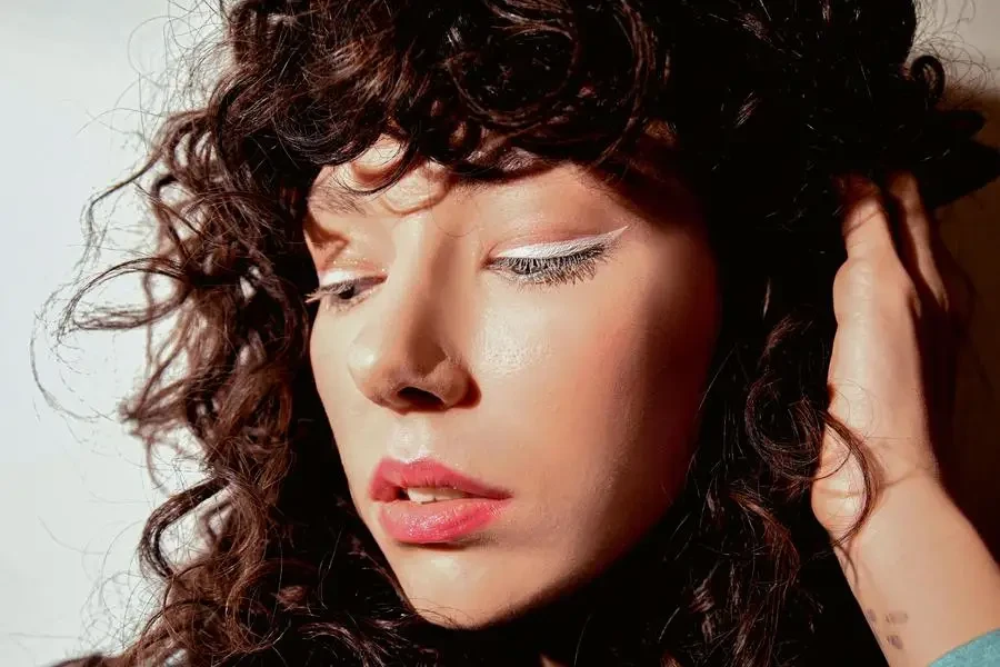 Studio Shot of a Young Woman with Curly Hair Wearing White Eyeliner by Konstantin Mishchenko