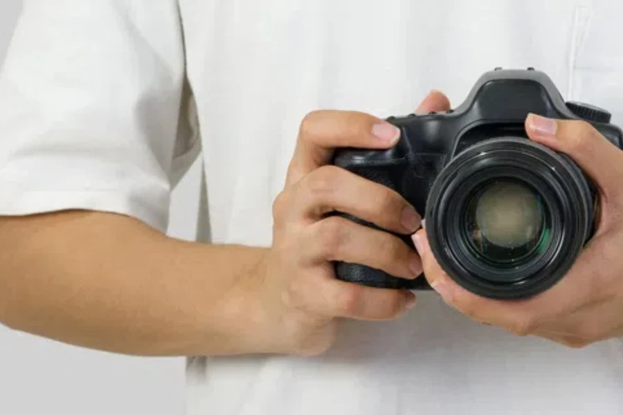 The photographer in white t-shirt holds camera by hand in the chest position