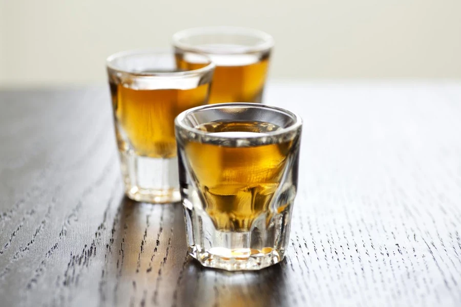 Three shot glasses full of dark colored alcohol on top of a bar table.