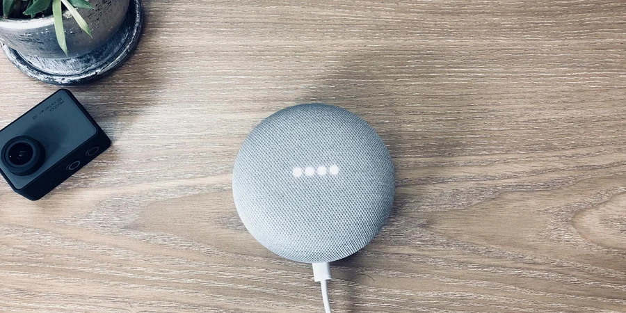 Top view of stylish smart speaker with connected white wire place on wooden table near small action camera and potted plant