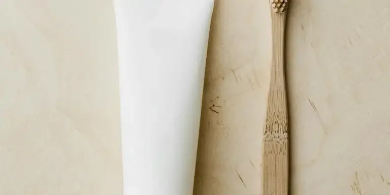 Top view of white mockup toothpaste tube and bamboo toothbrush placed on light brown wooden surface by Karolina Kaboompics