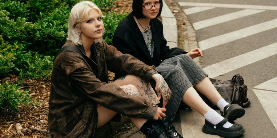 Two Young Women with Tattoos and Piercings Sitting on a Street in City